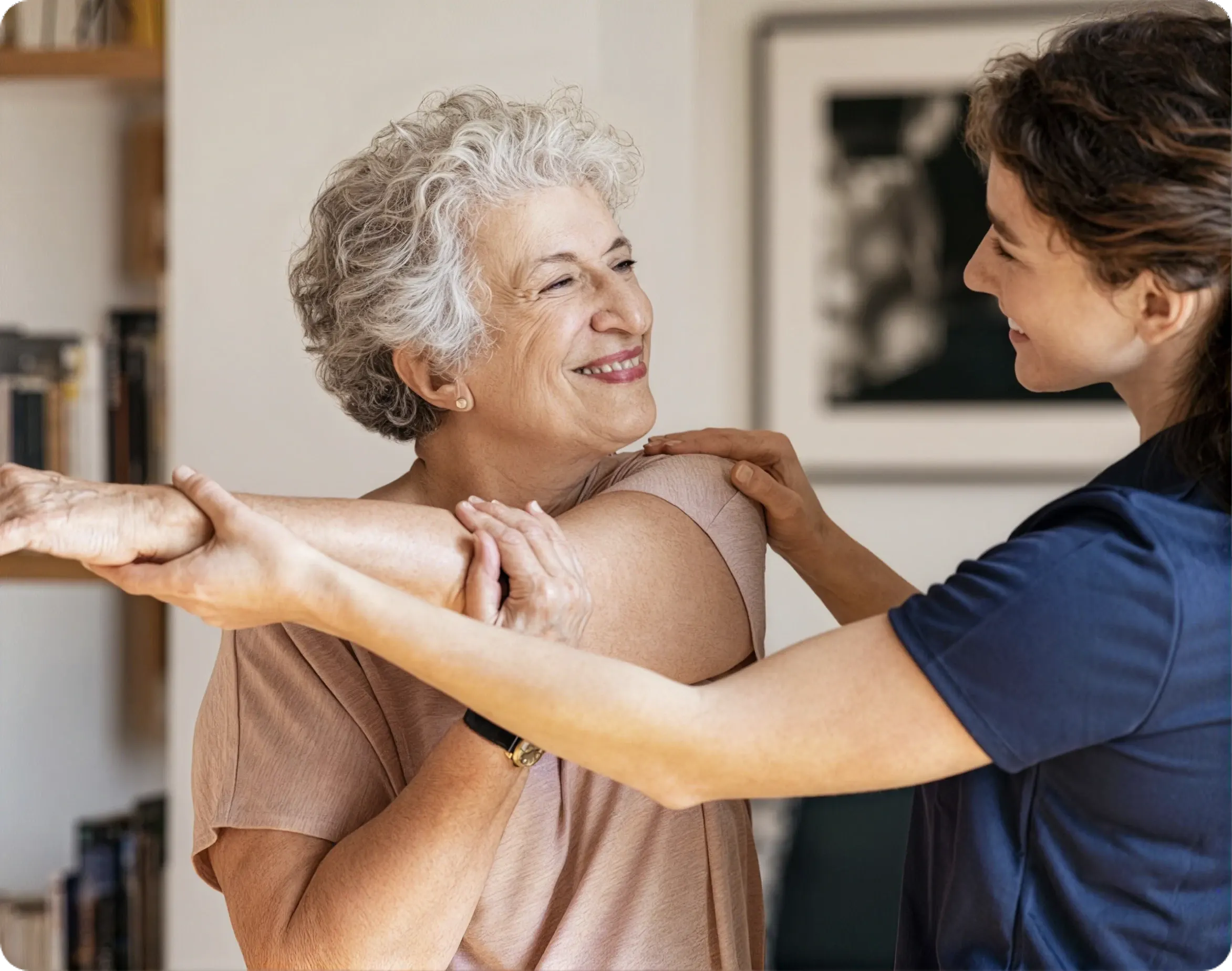 A caregiver helping an older woman stretch her arm during a session, smiling together