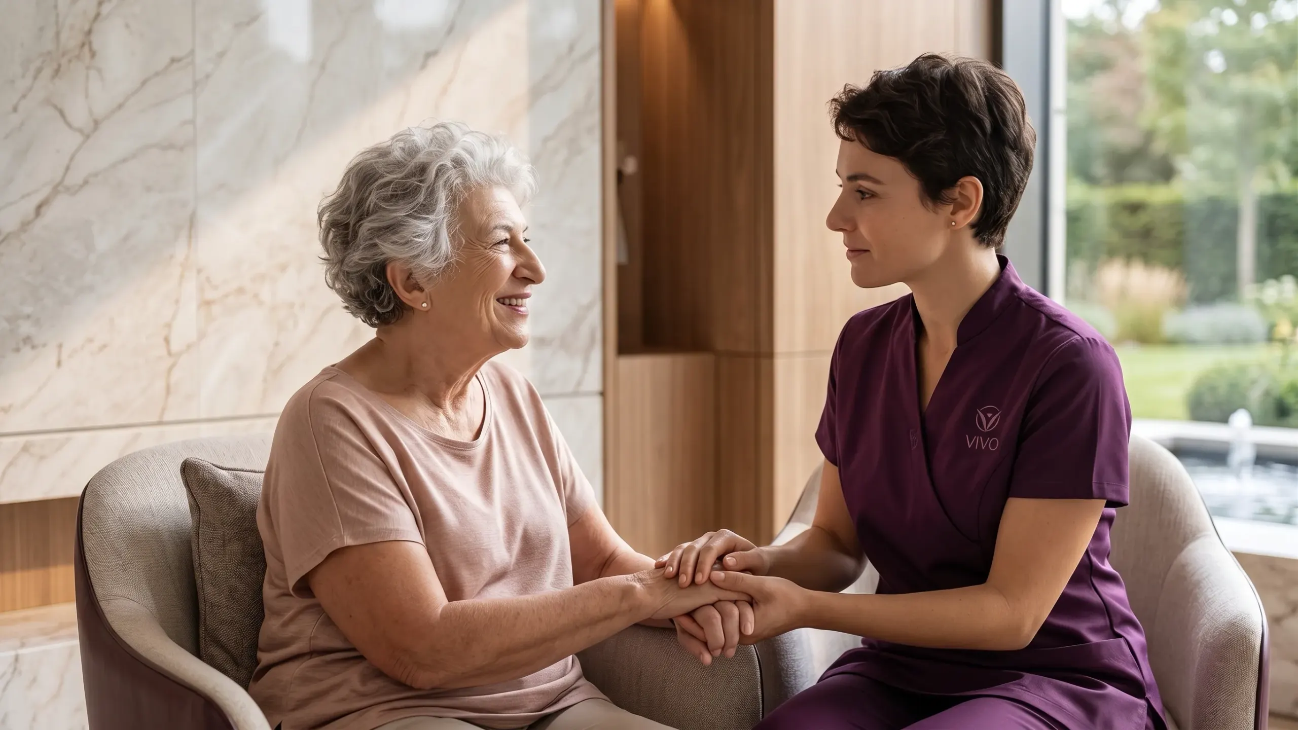 A Vivo Healthcare caregiver sitting with a resident, holding her hands